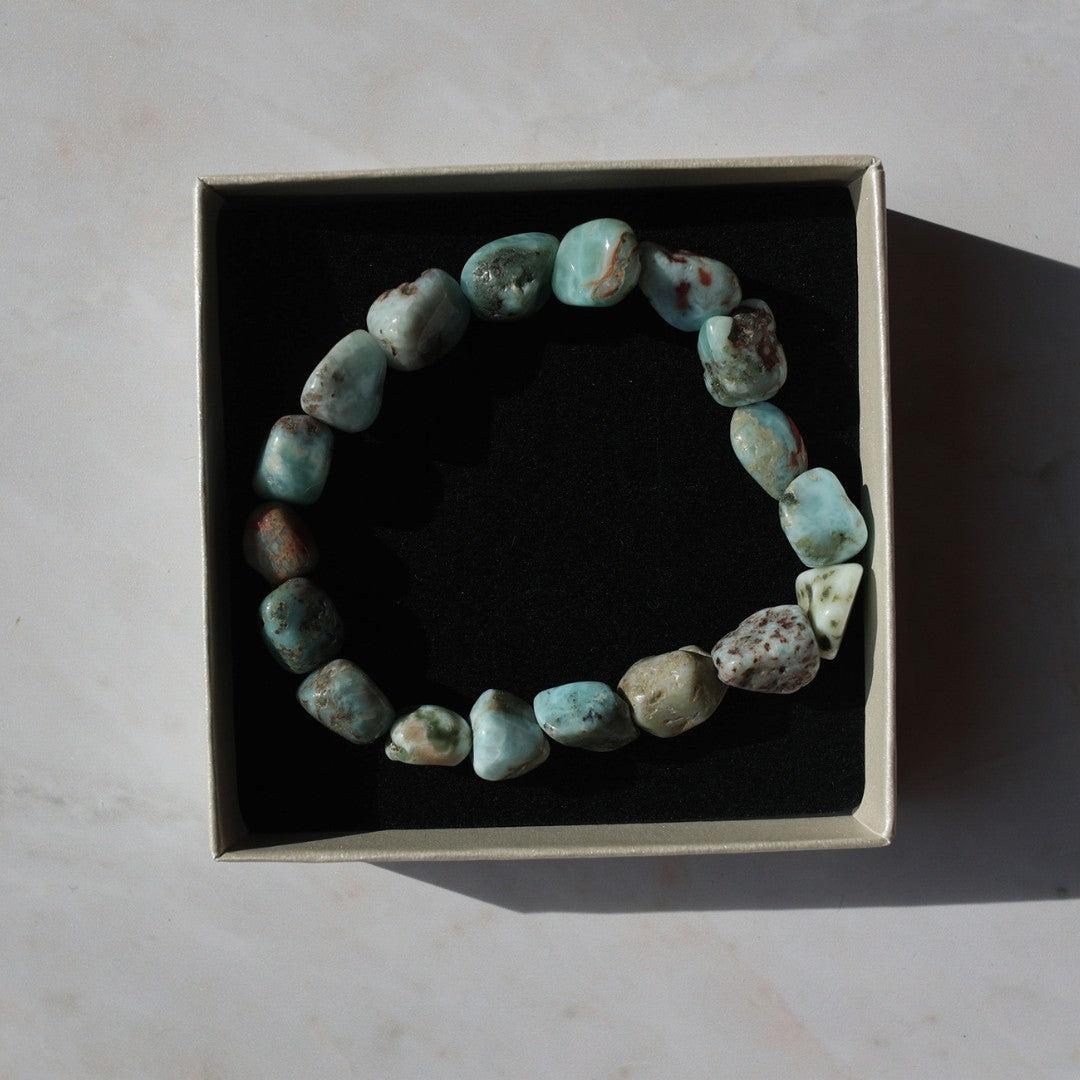 Larimar armbånd bestående af naturlige lyseblå og grønne sten præsenteret i en elegant kasse med sort indlæg