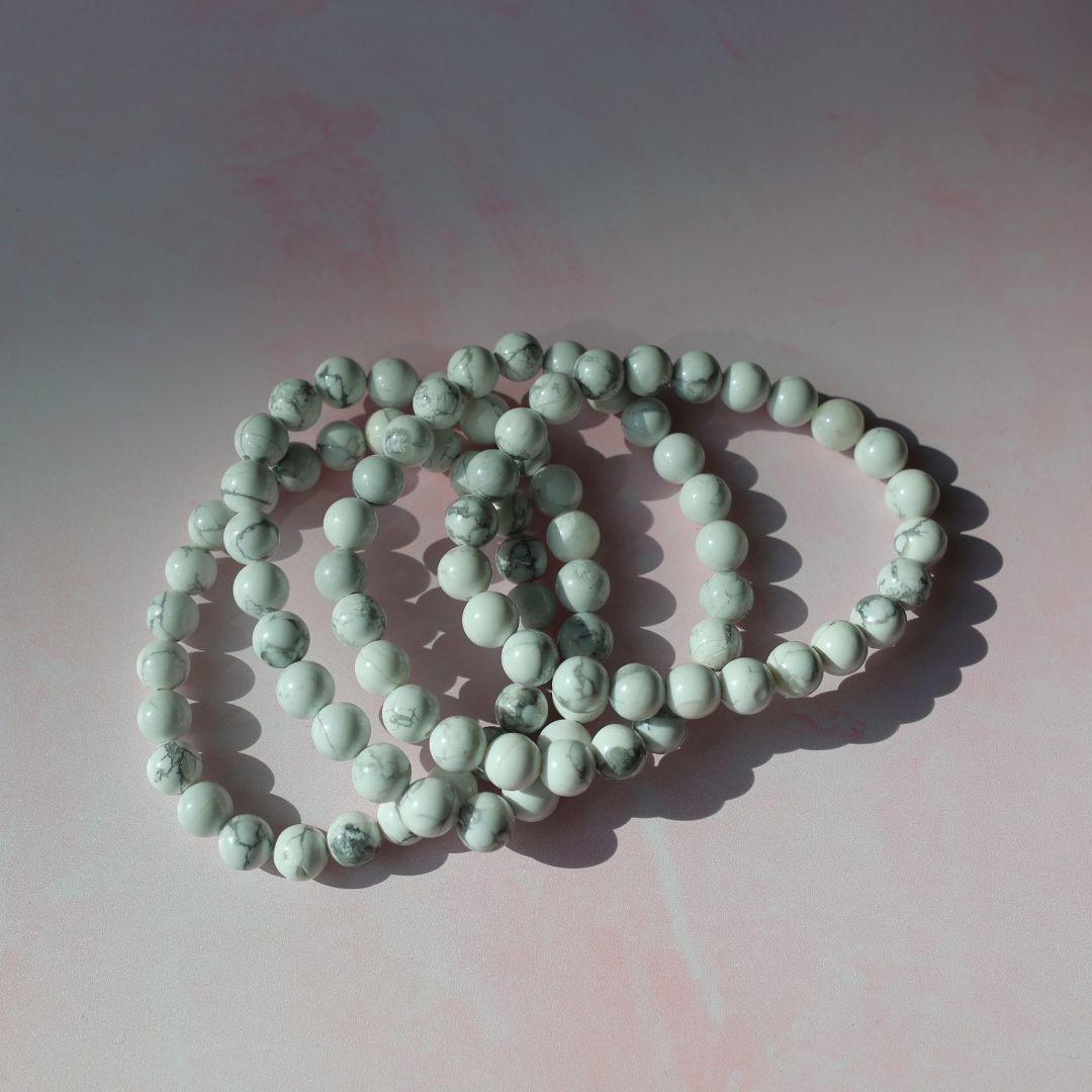Magnesit armbånd i forskellige størrelser og teksturer præsenteret på en lys pink baggrund med bløde skygger. Bead designet er i nuancer af hvid og grå med en flot marmorering.