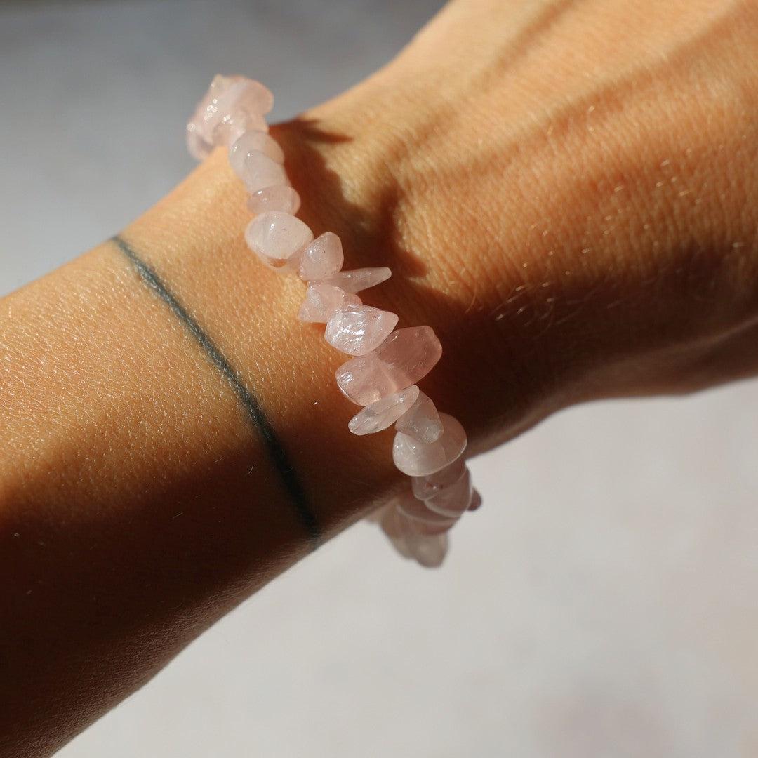Rosakvarts armbånd i lyserøde perler vist på en hånd med sollys der rammer armbåndet