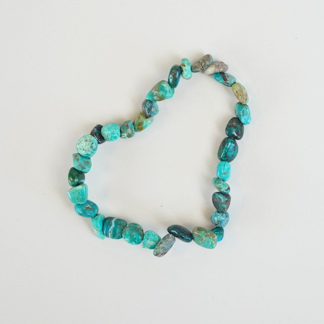 Chrysocolla armbånd med varierede nyancer af blå og grønne sten arrangeret i en hjerteform på en lys baggrund