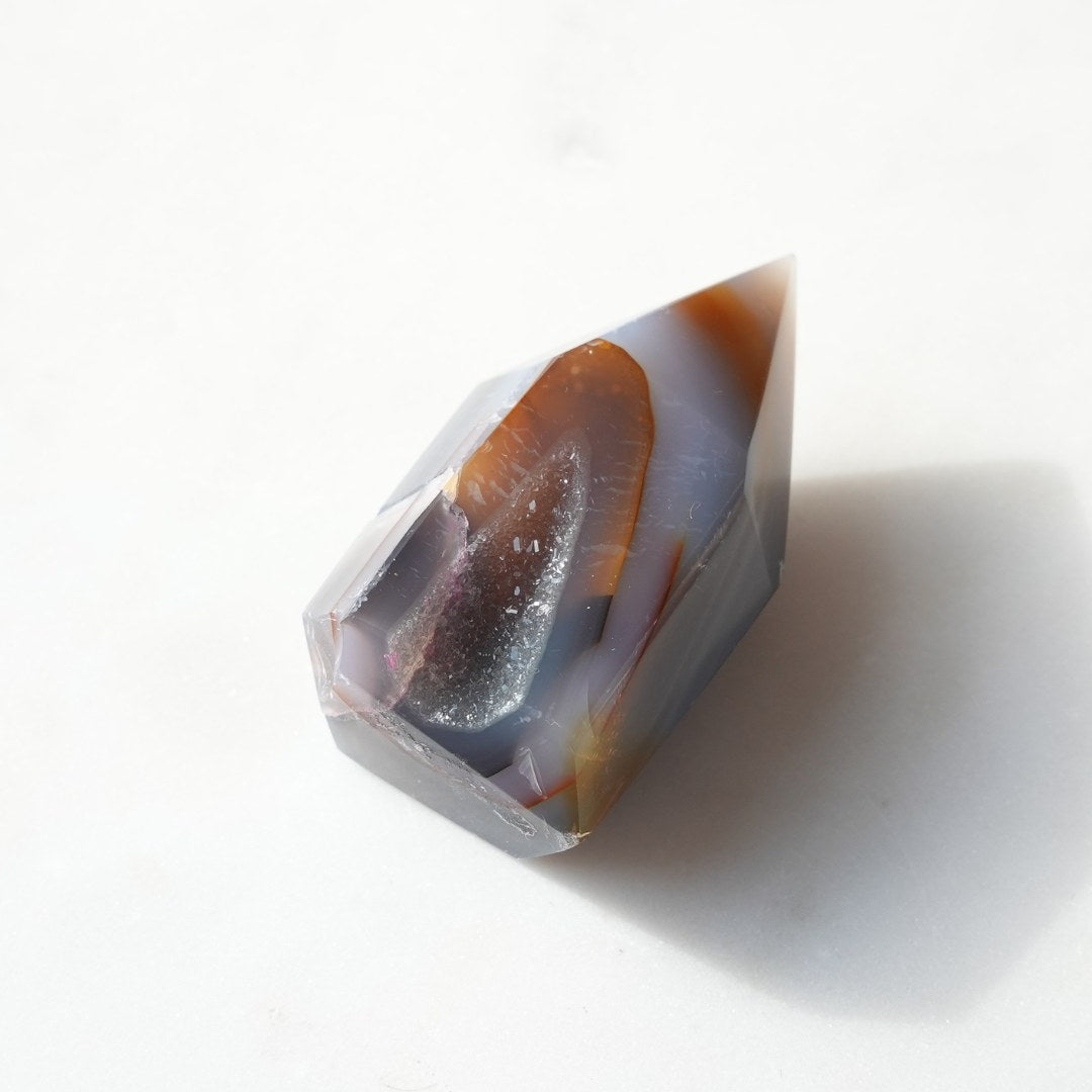 Druzy agat tårn med nuancer af grå, orange og en glitrende krystaloverflade som fremtræder i en spids form på en lys baggrund