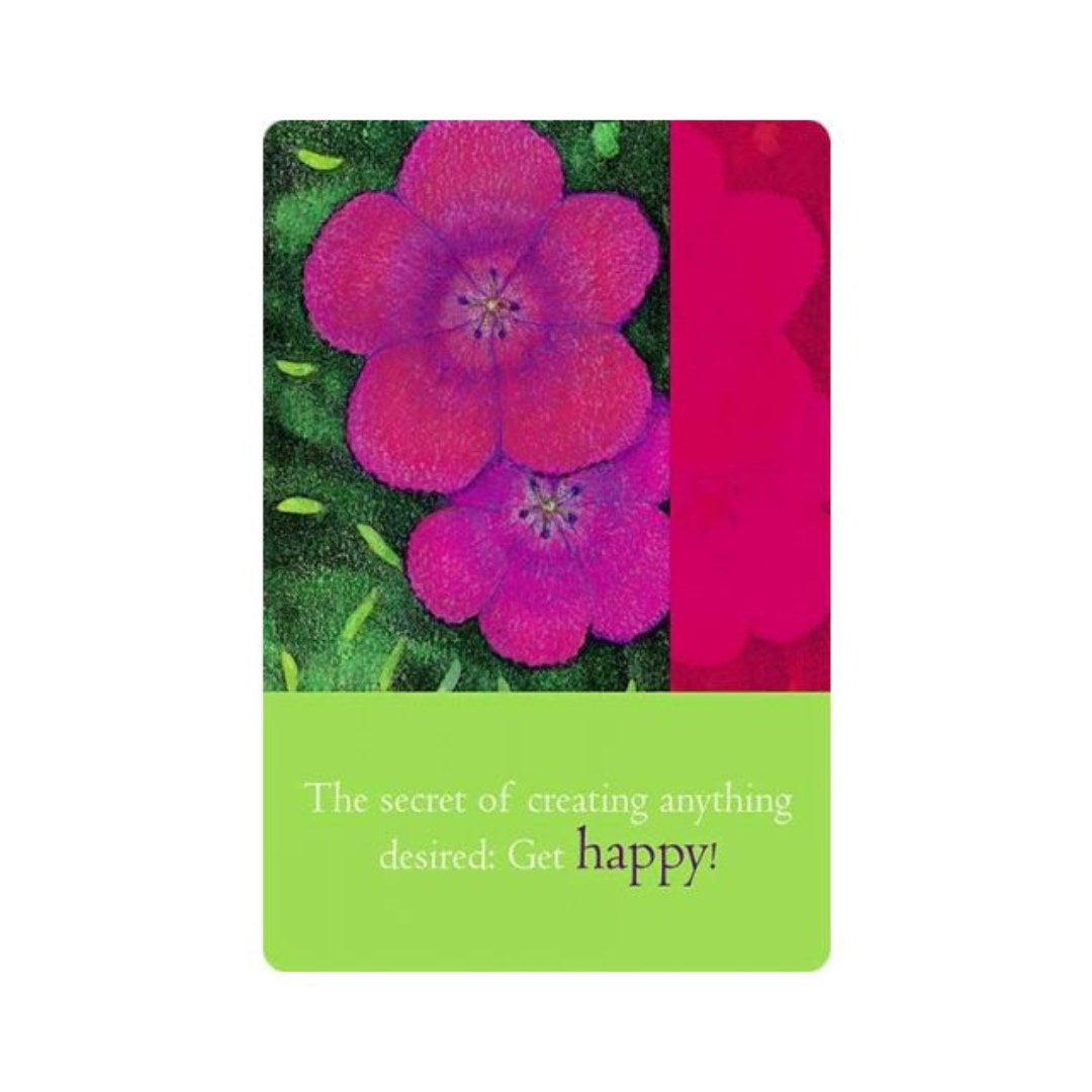 Kortet viser farverige blomster i nuancer af pink og lilla mod en grøn baggrund. Nederst står der en sætning i grøn tekst, der opfordrer til at være lykkelig.