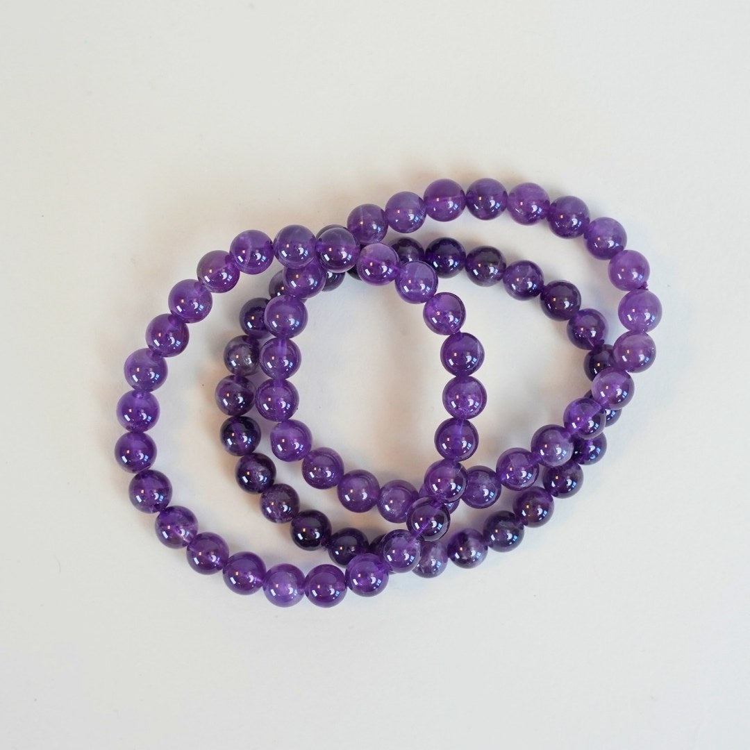Ametyst armbånd med 8 mm perler i lilla nuancer samlet i en elegant cirkel på hvid baggrund