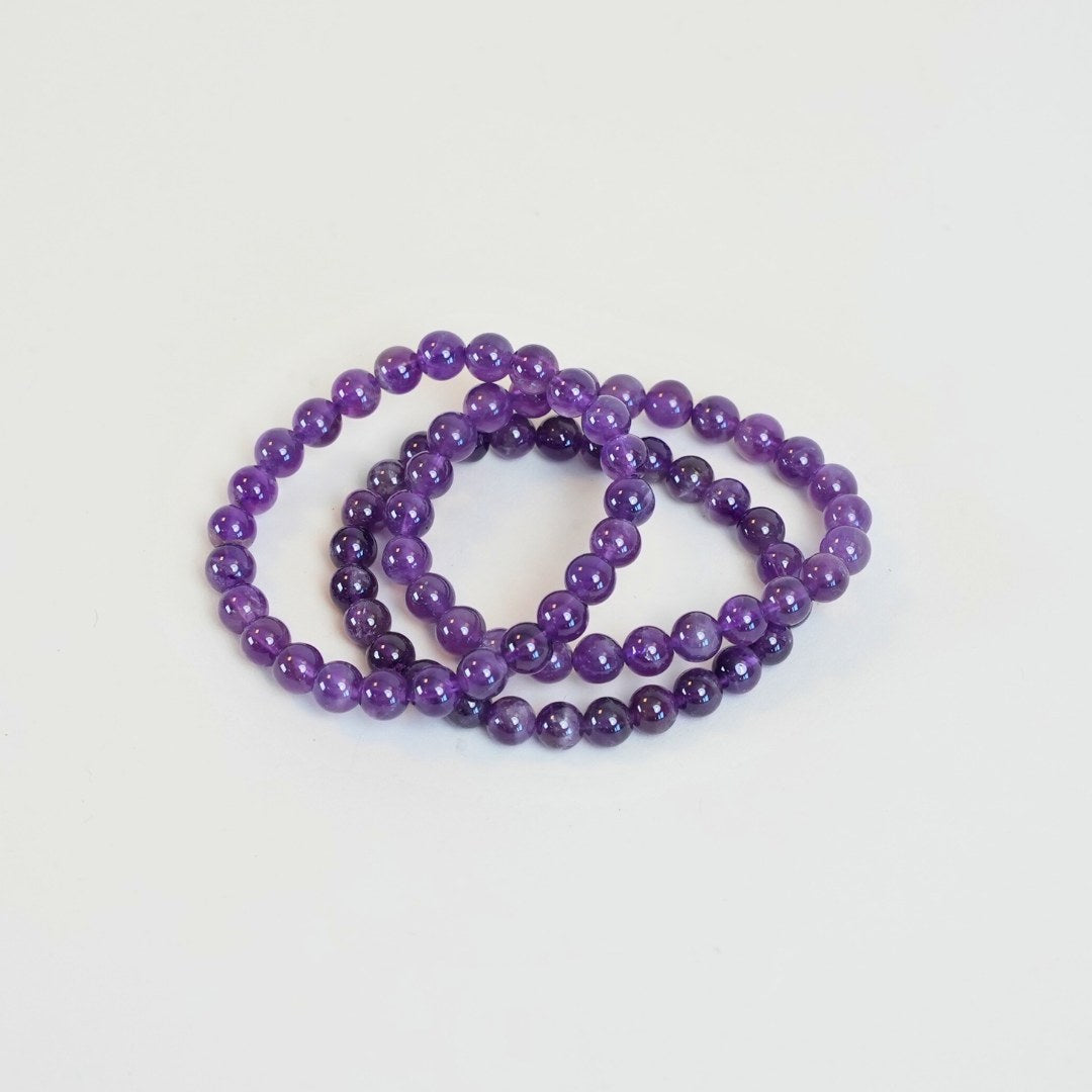 Ametyst armbånd med 8 mm perler i forskellige nuancer af lilla samlet i tre lag på en hvid baggrund