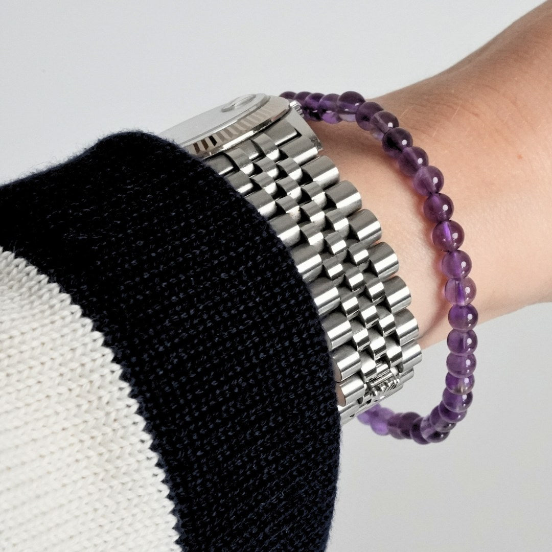 Ametyst armbånd i 4 mm perler på håndleddet af en person iført en sort og hvid striktrøje og et sølvur