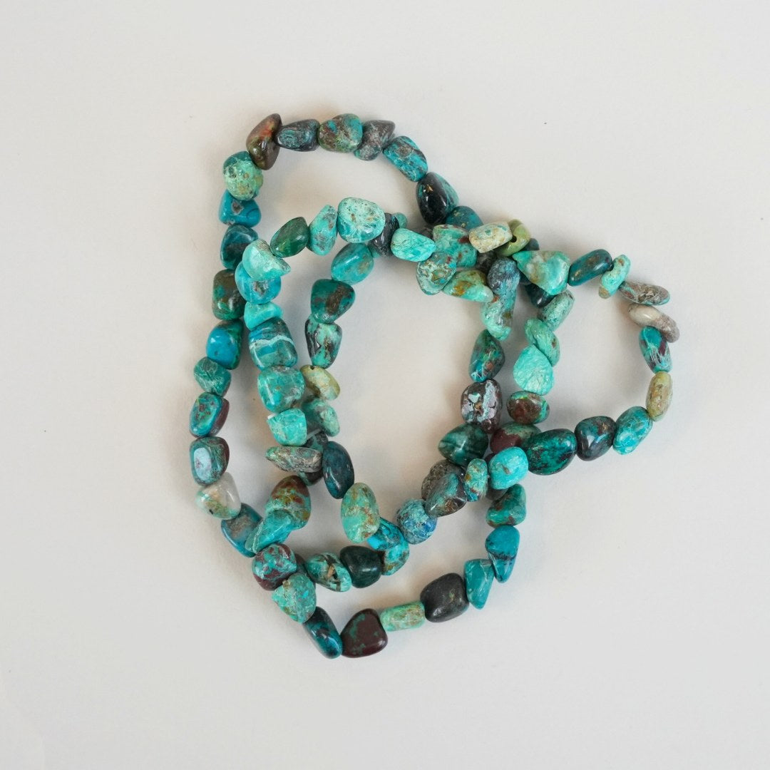 Chrysocolla armbånd lavet af farverige, polerede stykker af chrysocolla i nuancer fra blå til grøn med sorte og brune indslag arrangeret i et flettet design på en lys baggrund