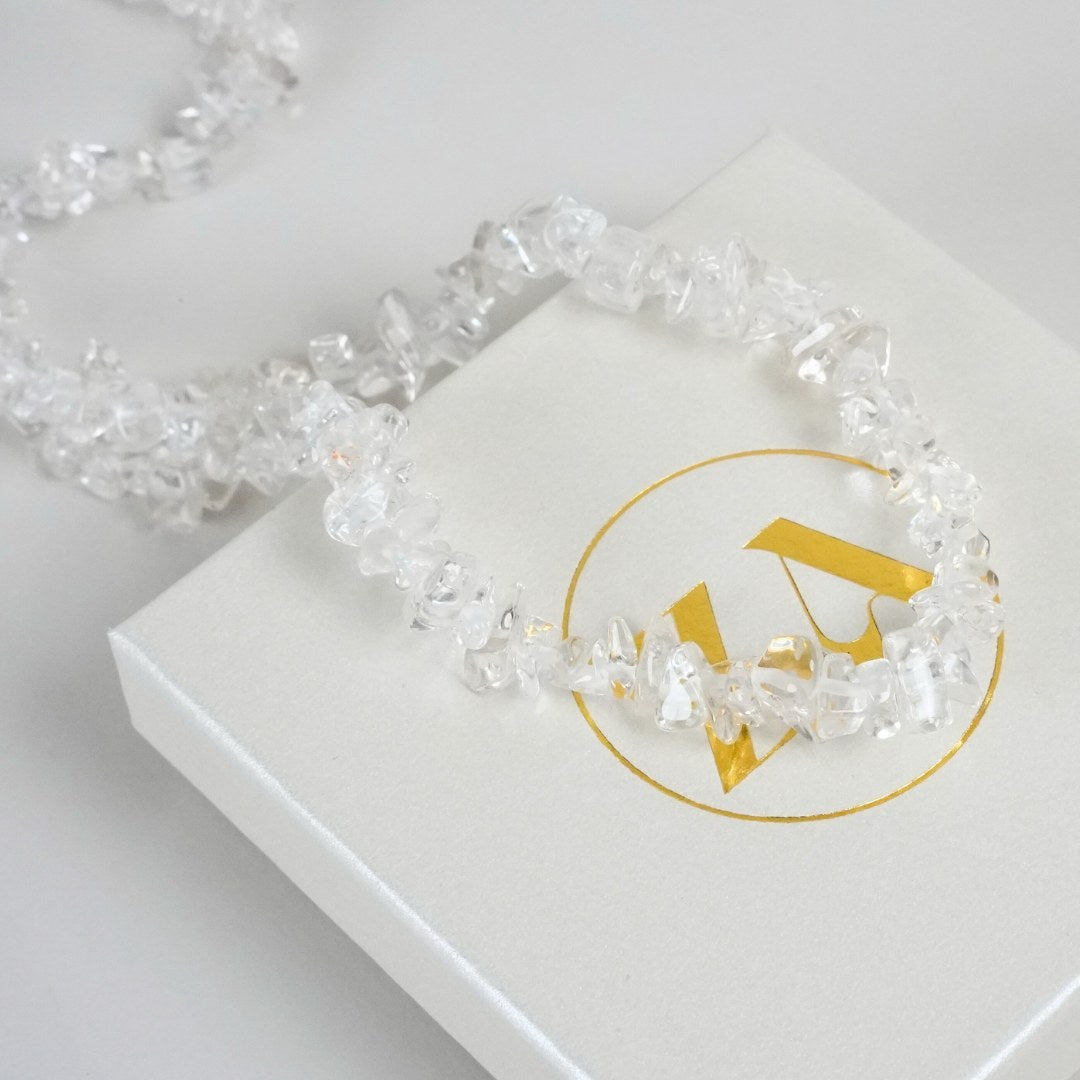 Bjergkrystal halskæde i klart lys med ujævne perler placeret rundt om en hvid gaveæske med guld logo