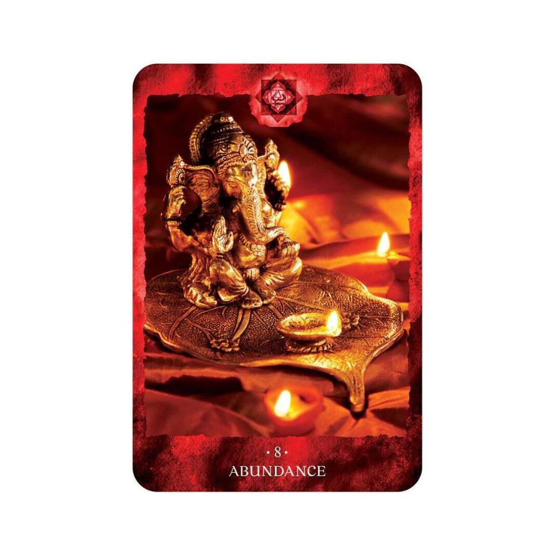 Billede af en orakelkort med en gylden skulptur af Ganesha på en dekoreret plade omgivet af små tændte stearinlys på en rød baggrund teksten nederst på kortet angiver nummer 8 og ordet overflod