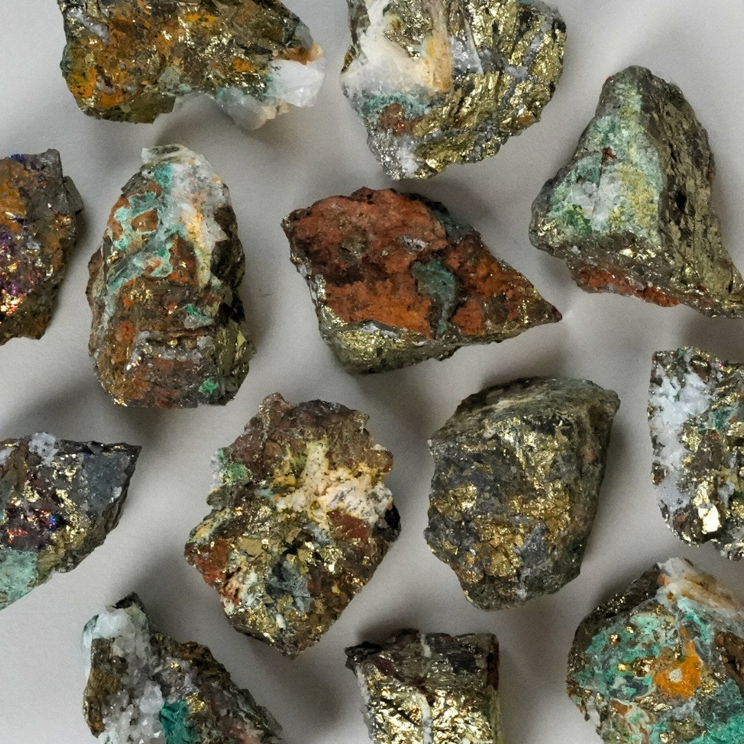 Billede af små stykker chalcopyrit rå med glinsende, metallisk overflade i nuancer af guld, grøn og brun spredt på en lys baggrund