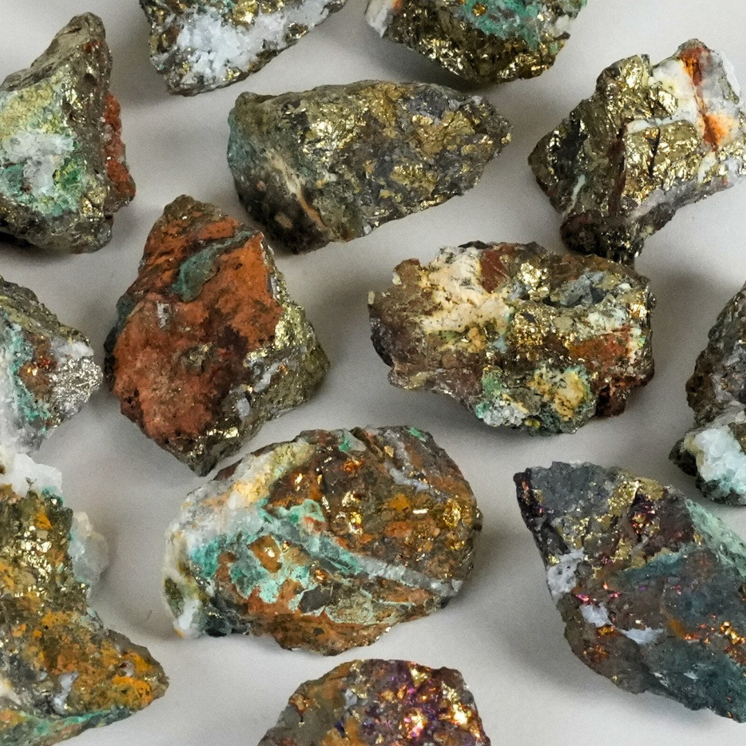 Chalcopyrite rå små sten i forskellige størrelse og former med gyldne og brune nuancer samt grønne og grå detaljer spredt ud på en lys baggrund