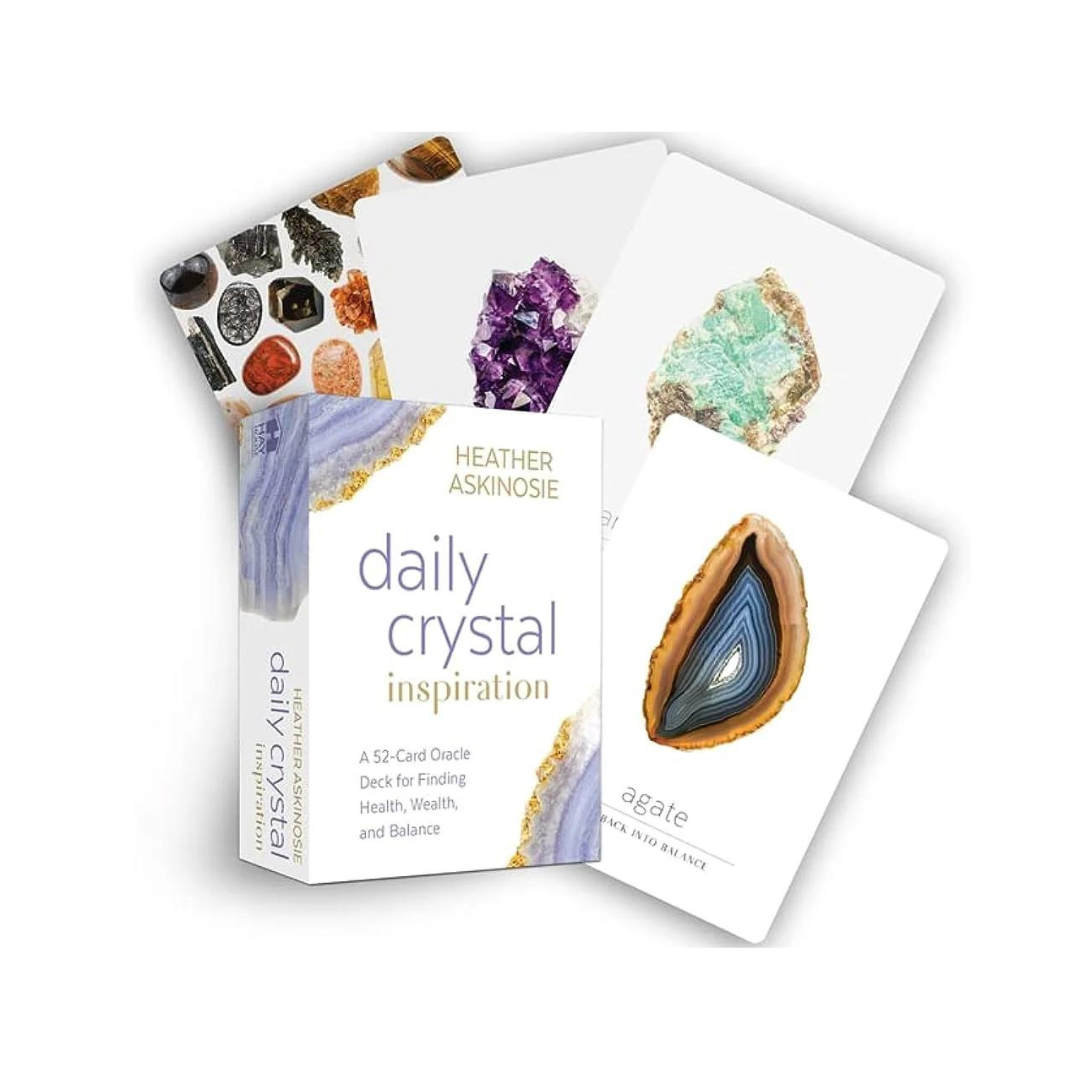 Billede af en æske med daglige krystalinspirations oraclekort med titlen Daily Crystal Inspiration af Heather Askinosie I baggrunden er der flere kort, der viser forskellige krystaller som ametyst, agater og akvamarin Æsken indeholder 52 kort til at finde sundhed, velstand og balance