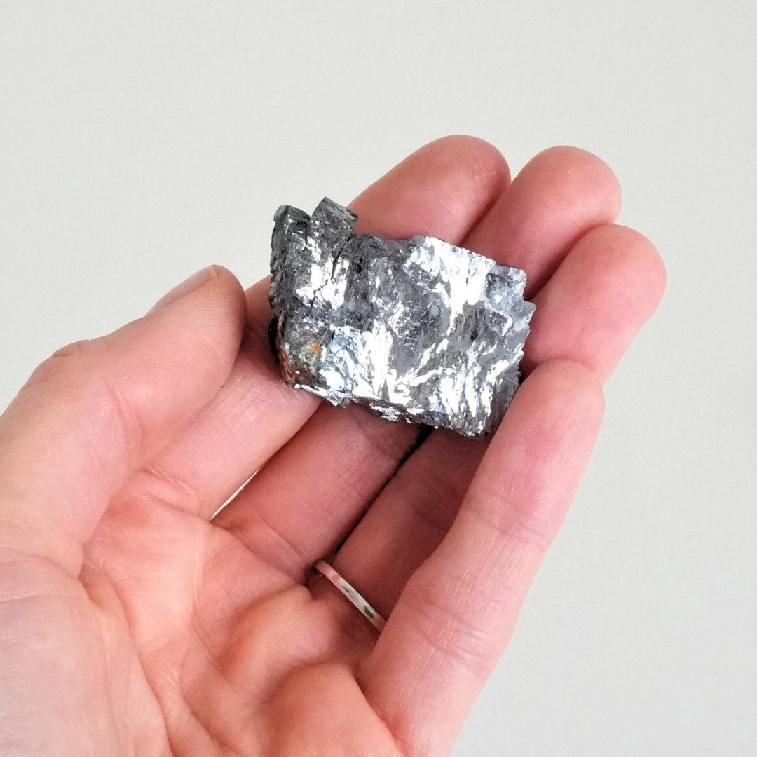 En person holder et stykke galenit i hånden det blanke mineral har en metallisk grå farve og en ujævn overflade