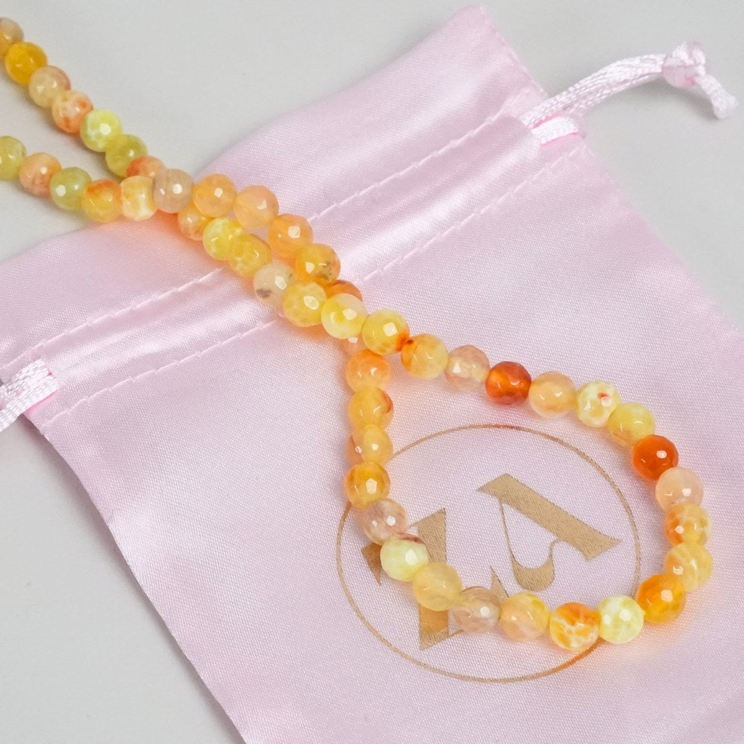 HOPE halskæde lavet af multifarvede perler i nuancer af gul og orange ligger på en pink satinsæk med et logo i guld.