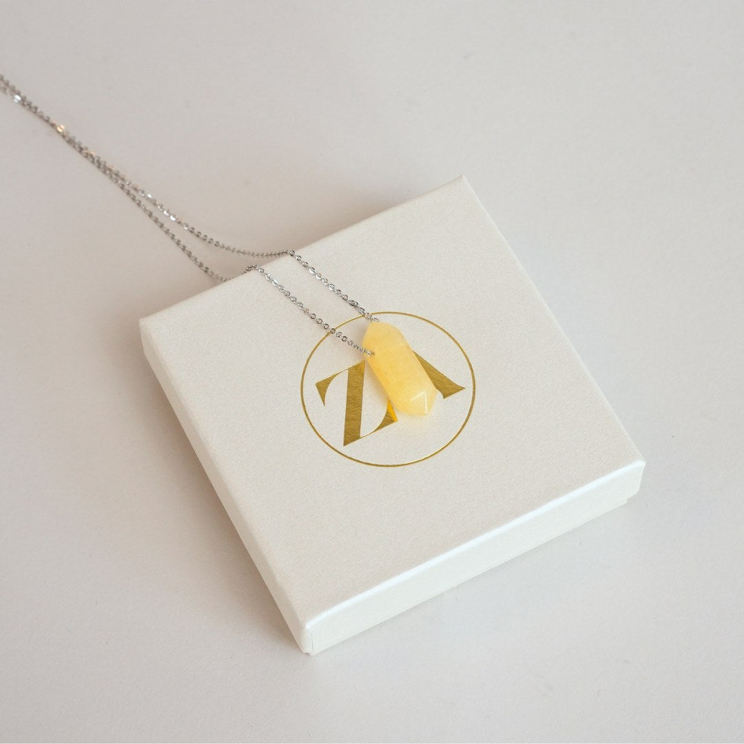 Gul aventurin halskæde hængende på en sølvkæde over en hvid smykkeæske med et gyldent logo på toppen