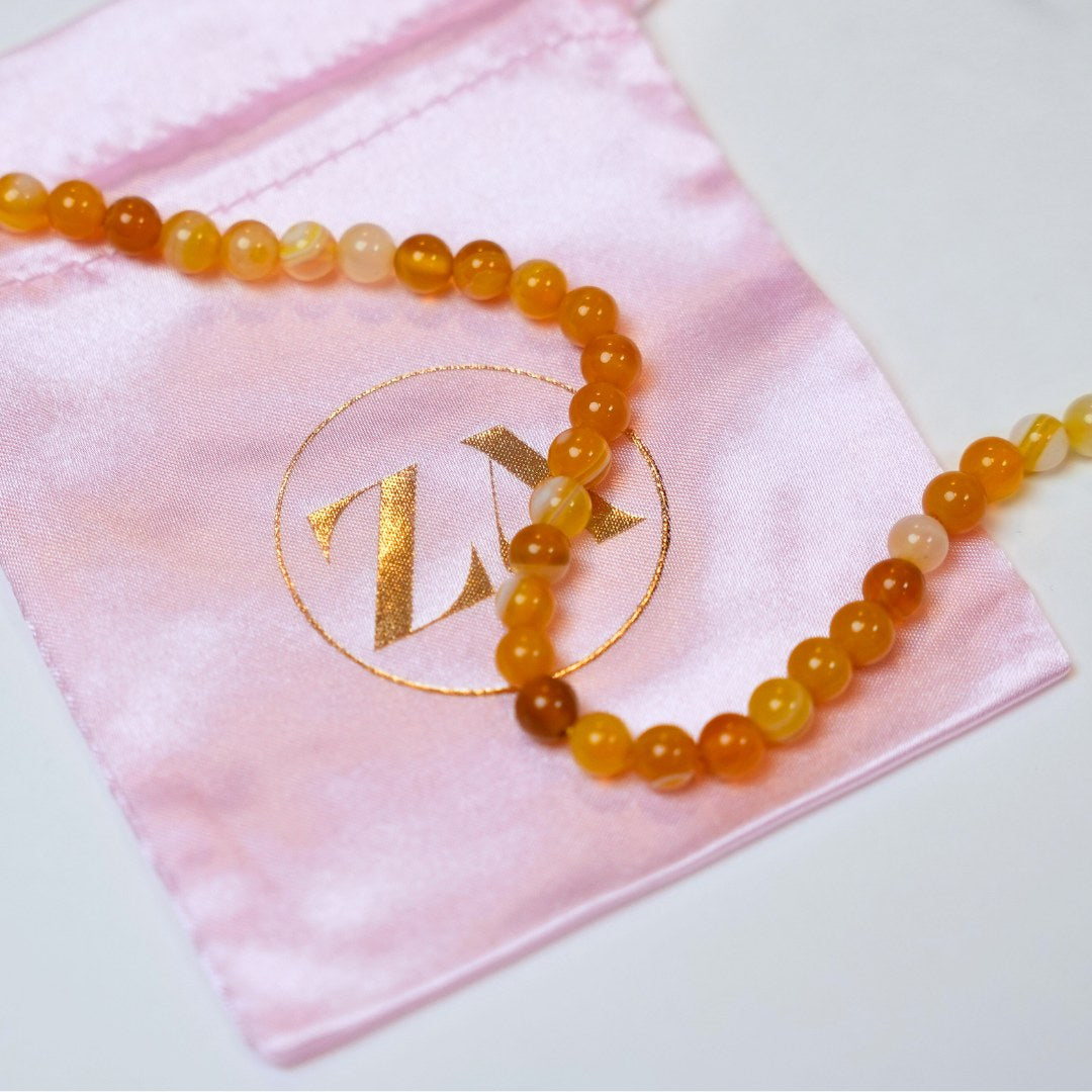 Solar plexus halskæde lavet af perler i nuancer af gul og orange præsenteret på en lyserød satinpose med guld-logo