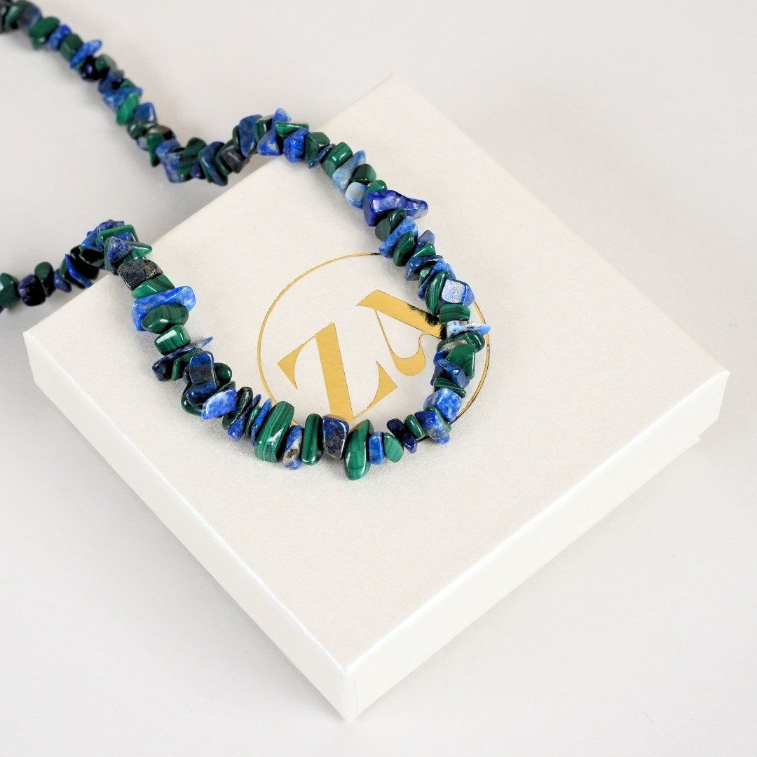 Malakit og lapis lazuli halskæde i en varieret sammensætning af grønne og blå sten præsenteret på en neutral gaveæske med et logo