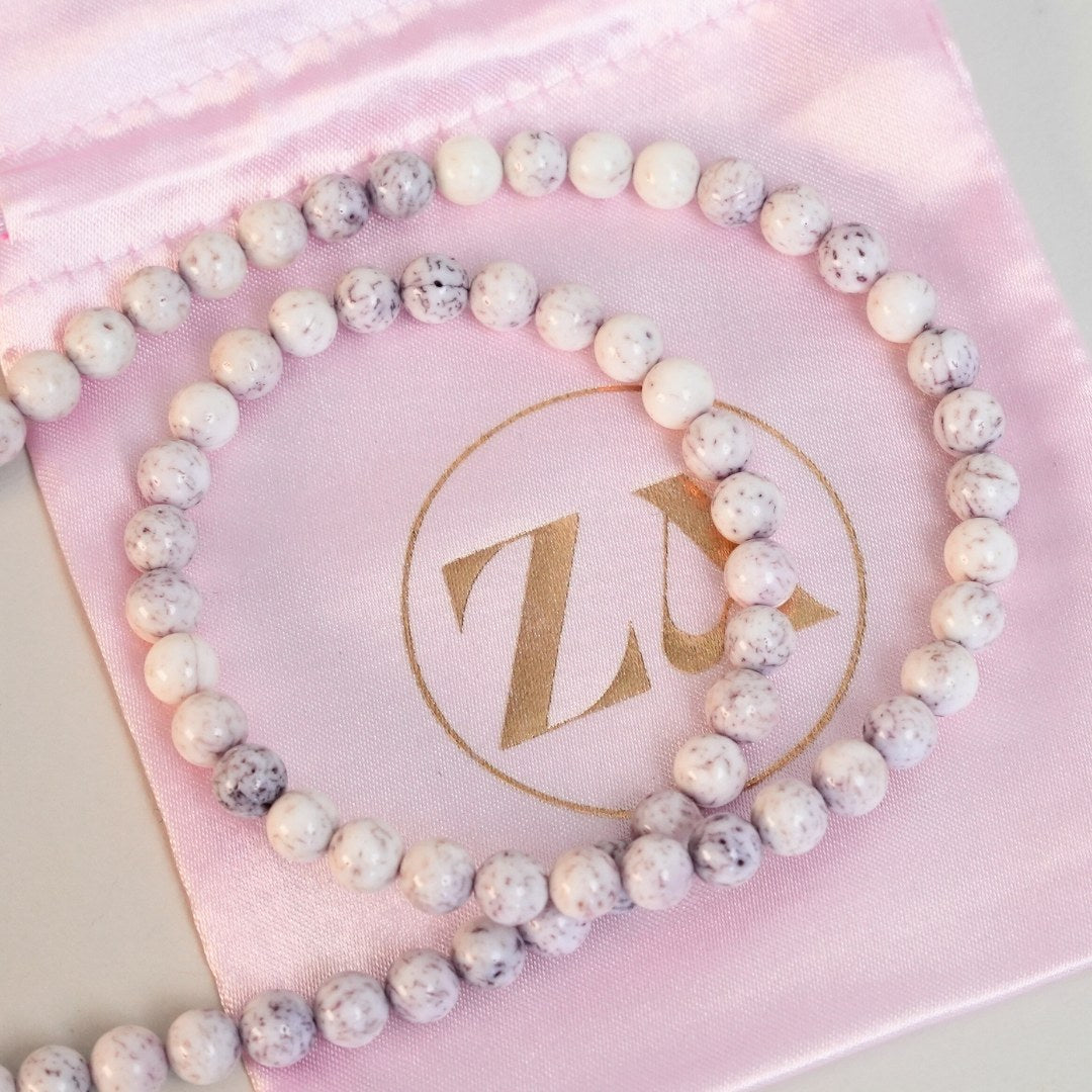 MAMA EARTH halskæde lavet af perler i lyserøde og hvide nuancer præsenteret på en lys pink stofpose med et gyldent logo