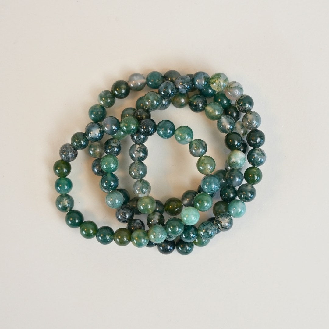 Mos agat armbånd bestående af flere lag med grønne og blå nuancer af glatte perler arrangeret i cirkler på en lys baggrund