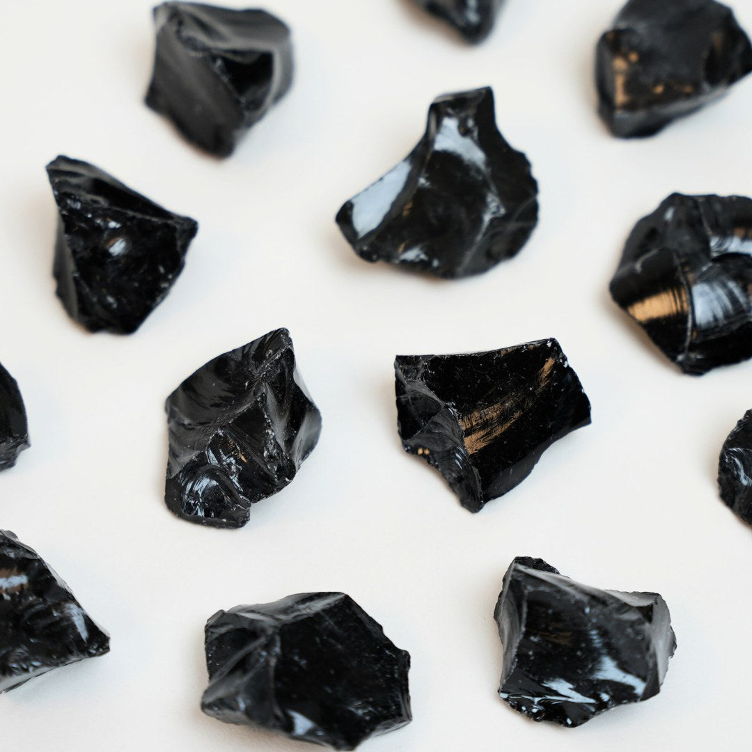 Obsidian rå krystaller af forskellig form og størrelse ligger på en lys baggrund med glinsende overflade og dyb sort farve