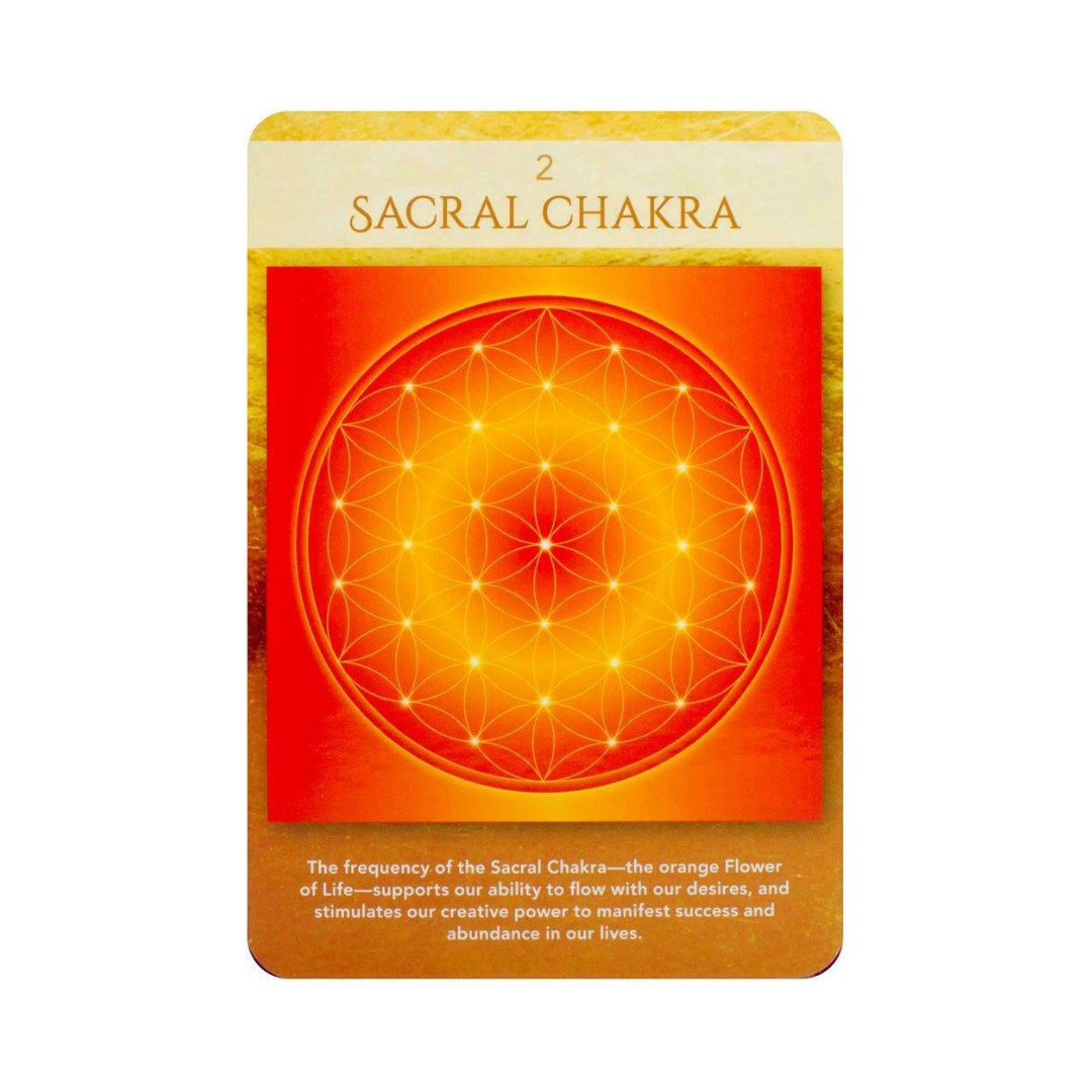 Et orakelkort med titlen Sacral Chakra viser en lys orange baggrund med et geometrisk mønster i midten. Mønstret, som ligner en blomsterform, har flere blændende lys, der symboliserer kreativitet og flow. Nederst på kortet er tekst, der beskriver kortets betydning og dets forbindelse til livets strøm og overflod.