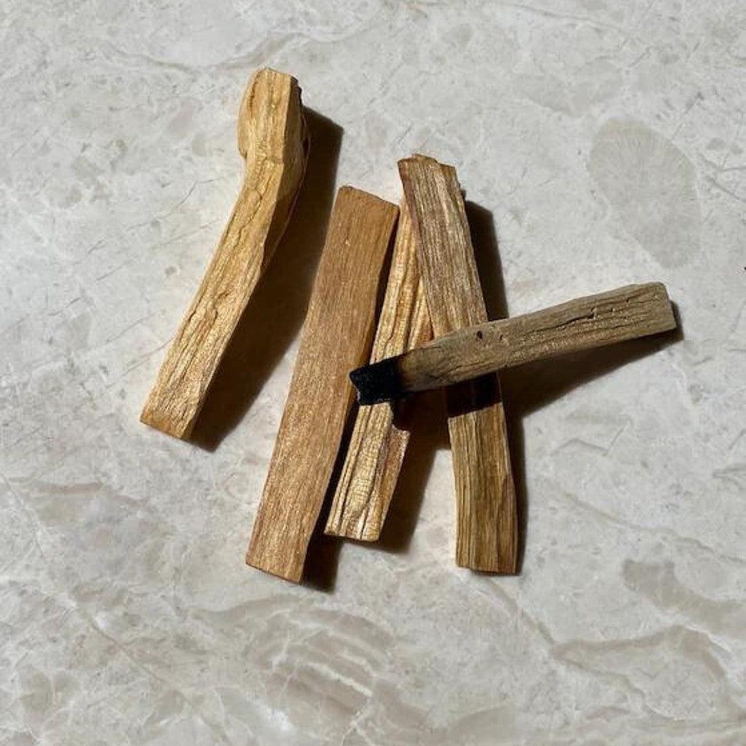 Billede af flere stykker palo santo træ lægges på en lys marmoroverflade træet har en gyldenbrun farve og en glat tekstur nogle stykker har en sort afslutning der indikerer at de er blevet brændt