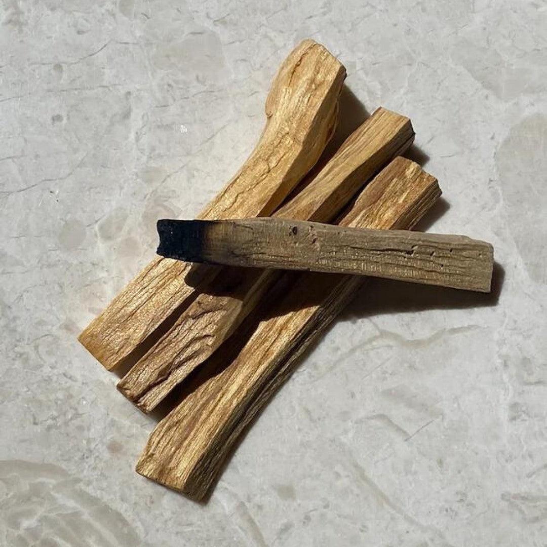 Billede af flere stykker palo santo træ i forskellige længder og tykkelser liggende på en lys marmoroverflade med en let brændt spids på et af stykkerne