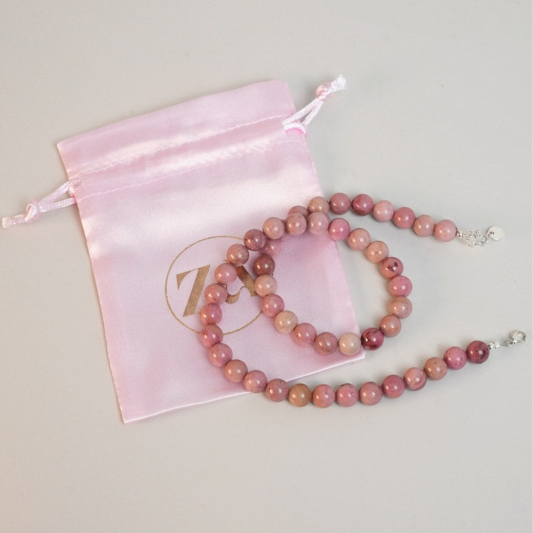 Et smukt LET GO halskæde lavet af farverige perler i nuancer af rosa og lyserød lagt sammen med en elegant lyserød silkepose med et guld-logo