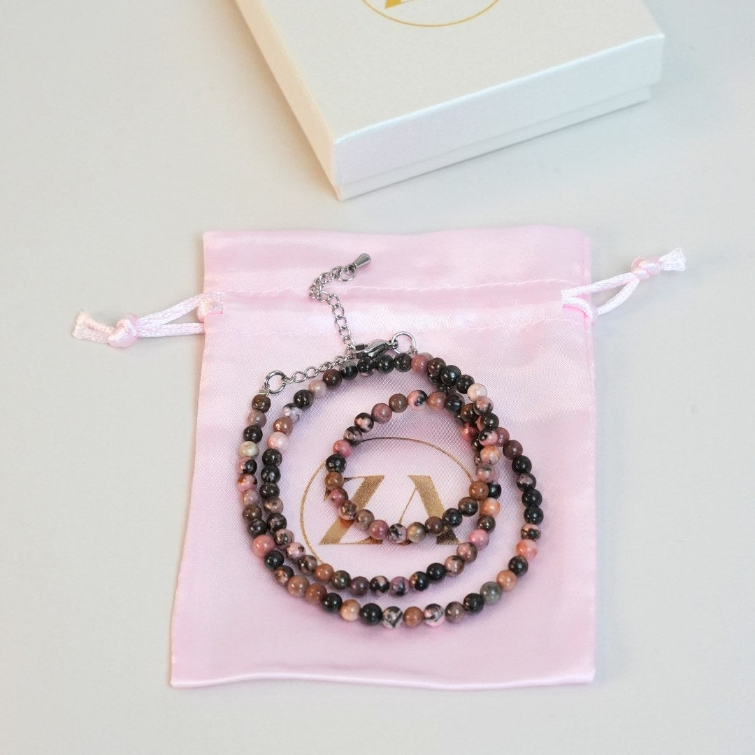 HEART halskæde i smukke perler i nuancer af rosa og sort præsenteret på en lyserød stofpose med snorelukning og et elegant logo i guld på posen