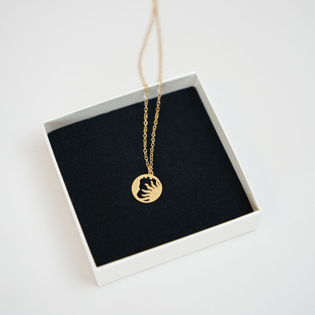 Guld halskæde med cirkulært vedhæng der forestiller en sol og måne i en smuk, enkel design præsenteret i en hvid smykkeboks med sort indlæg