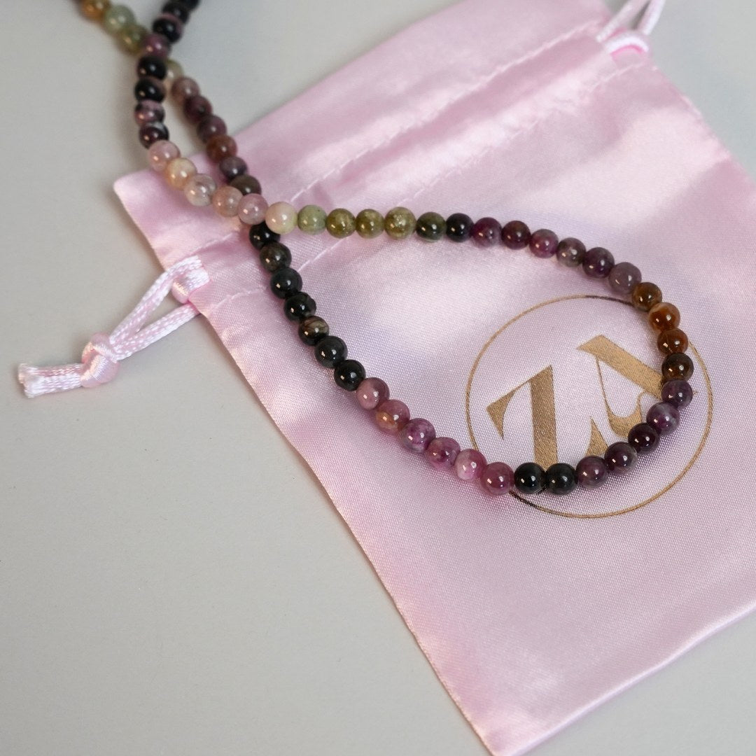 Wisdom halskæde i forskellige farver af perler ligger på en lyserød silkepose med et guld logo