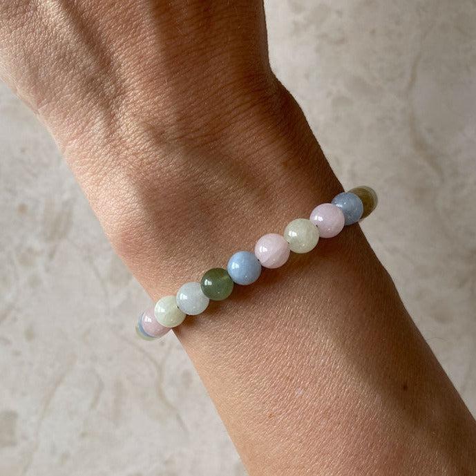 HEALING LOVE armbånd med farverige perler på en hånd med en neutral baggrund