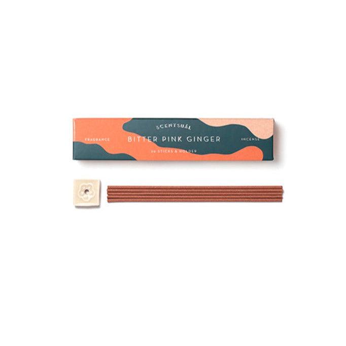 Bitter pink ginger fra Scentsual præsenteres med en elegant emballage i grøn og orange nuancer indeholdende røgelsespinde og en hvid holder formet som en blomst.