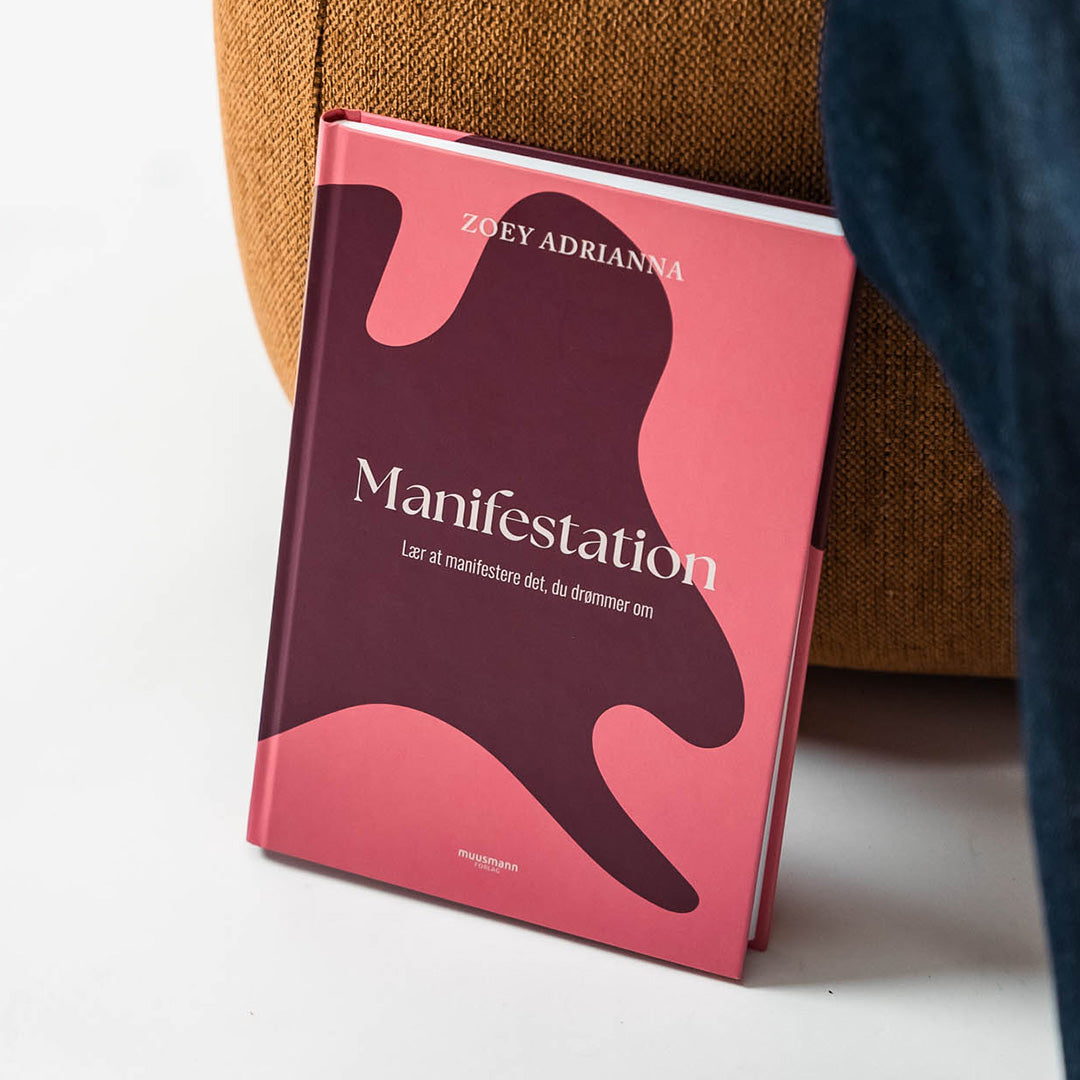 Bok med titeln Manifestation av Zoey Adrianna placerad nära en soffa